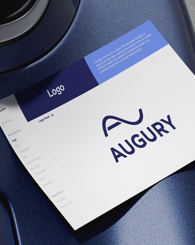 Angled AUGURY brand-guidelines page with a navy logo on a white sheet over a dark blue surface.