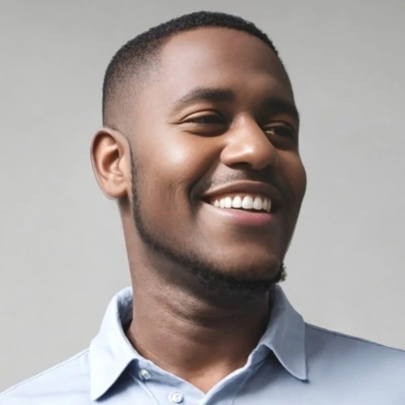 Smiling man with short hair and a beard wearing a light blue collared shirt against a gray background.