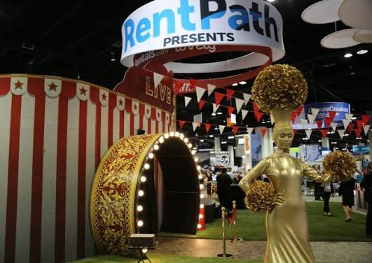 Gold-painted statue and illuminated ornate arch beneath “RentPath PRESENTS” signage in a red-and-white booth.